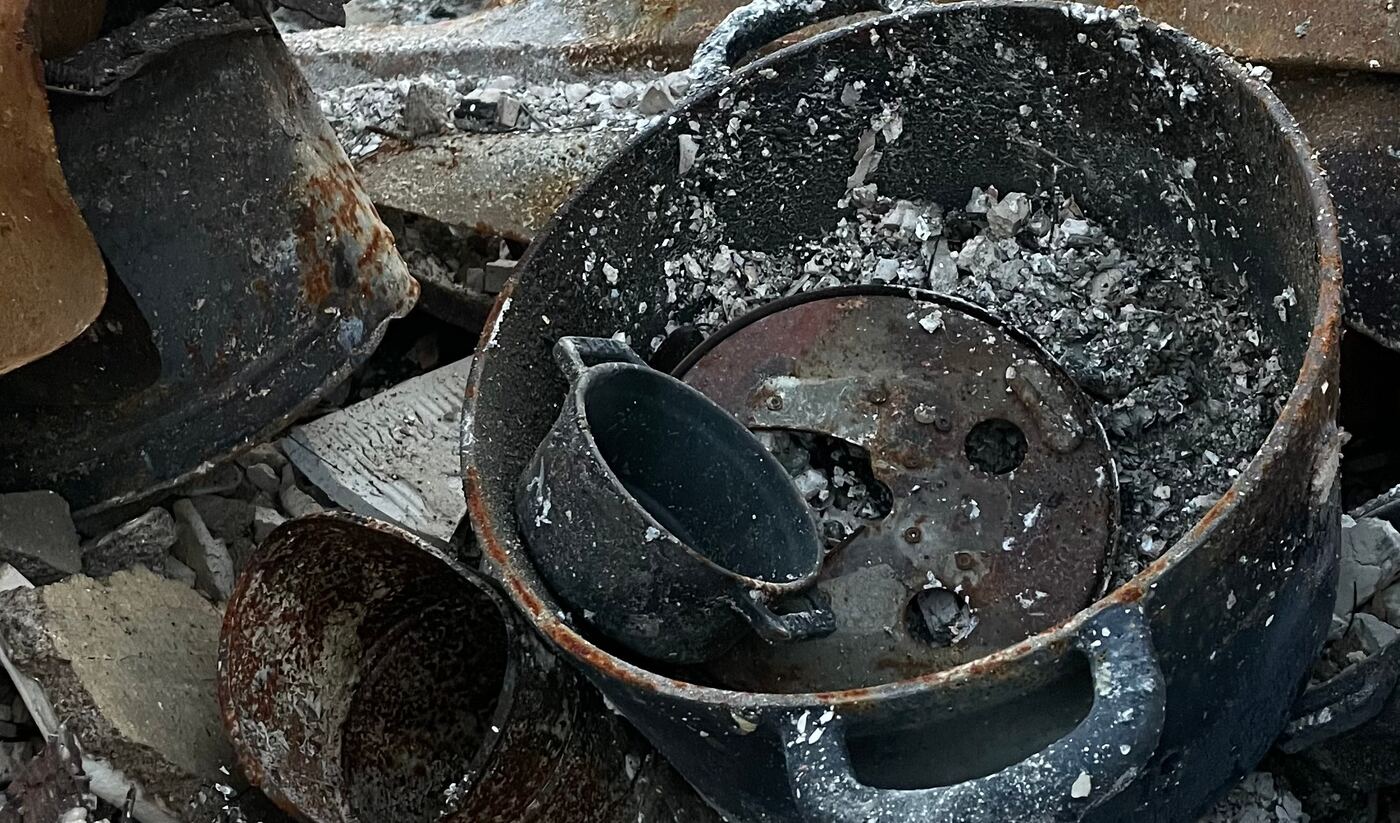 A charred cooking pot filled with ash and broken debris sits in the burned wreckage of the home.
