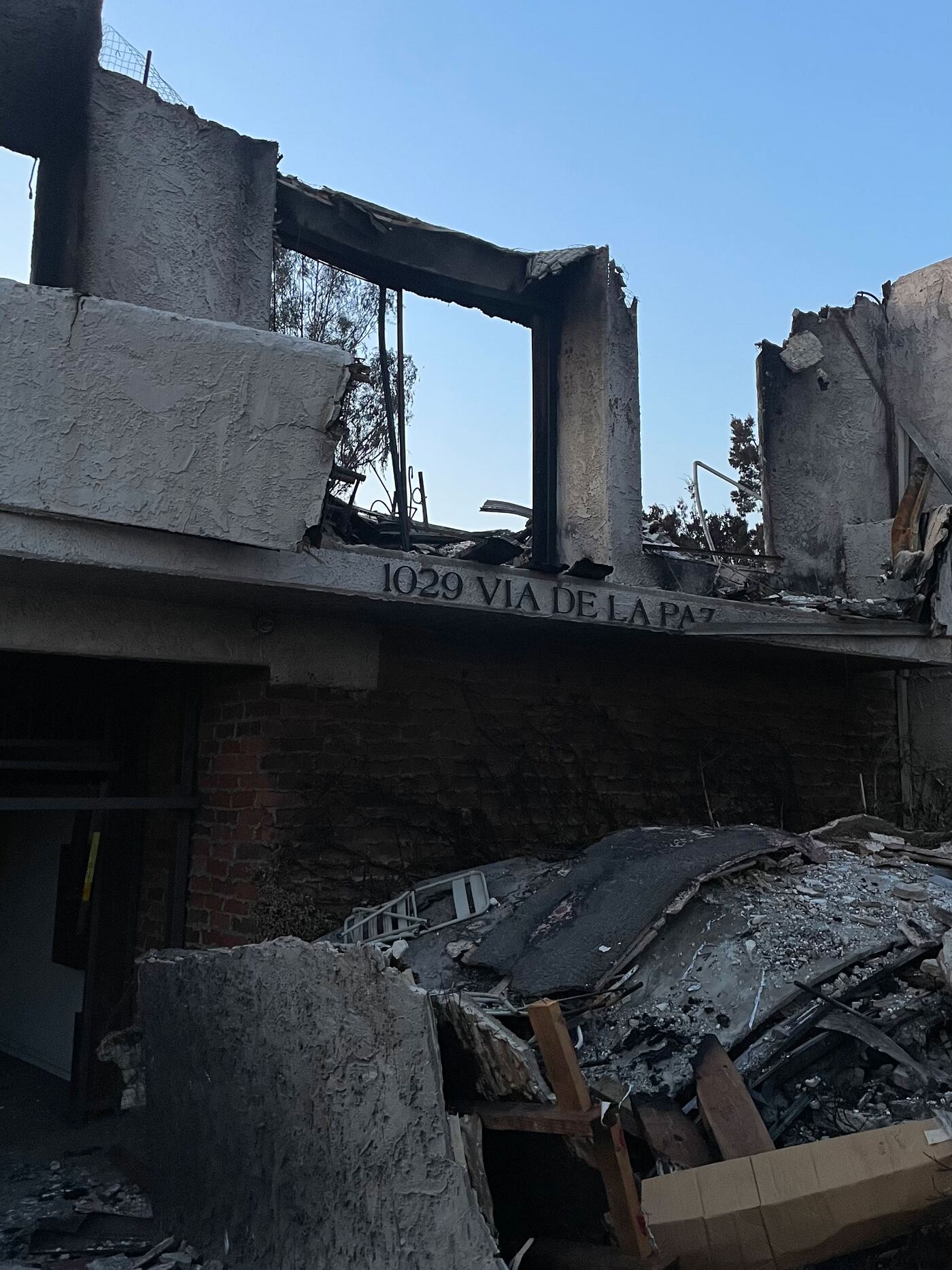 The scorched facade of the building at 1029 Via de la Paz, its address still legible above a collapsed roof and burned stairwell.